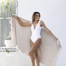 alt="A woman holding a stylish natural beach towel with a small check pattern achieved through a series of high and low sections of towelling finished with a beautiful fringe along the ends"