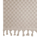 alt="Close-up view of a stylish natural beach towel with a small check pattern with a beautiful fringe along the ends"