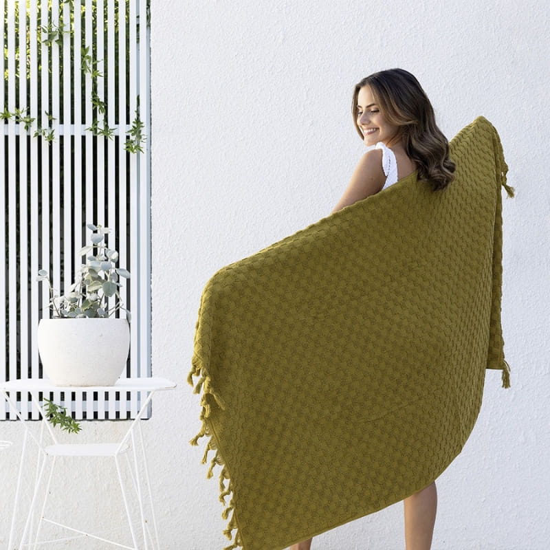 alt="A woman holding a stylish moss green beach towel with a small check pattern achieved through a series of high and low sections of towelling finished with a beautiful fringe along the ends"