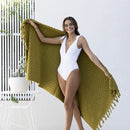 alt="A woman holding a stylish moss green beach towel with a small check pattern achieved through a series of high and low sections of towelling finished with a beautiful fringe along the ends"