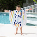 A little girl wrapped in a vibrant little nipper poncho, enjoying a sunny day at the beach.