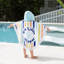 A little girl in a vibrant shaped little nipper poncho towel by the pool, enjoying a sunny day while staying warm.