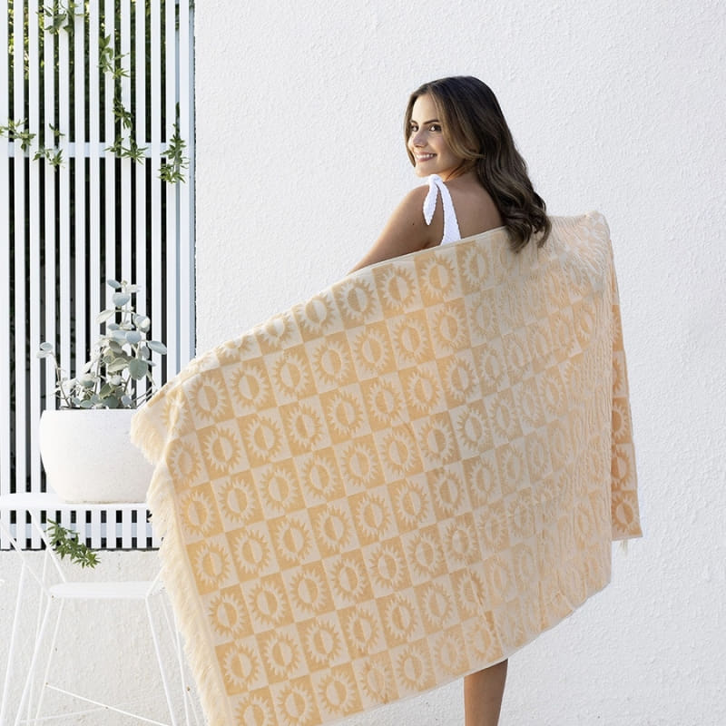 alt="A woman holding a yellow beach towel featuring a stylish sun pattern with knotted tassels on both ends"