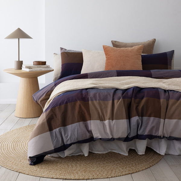 The quilt cover set features a large check design in purple, navy, and beige tones. Made of high-quality, yarn-dyed cotton fabric, it adds sophistication to any bedroom.