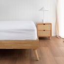 Fitted white cotton sheet on a timber bed frame next to a rattan bedside table