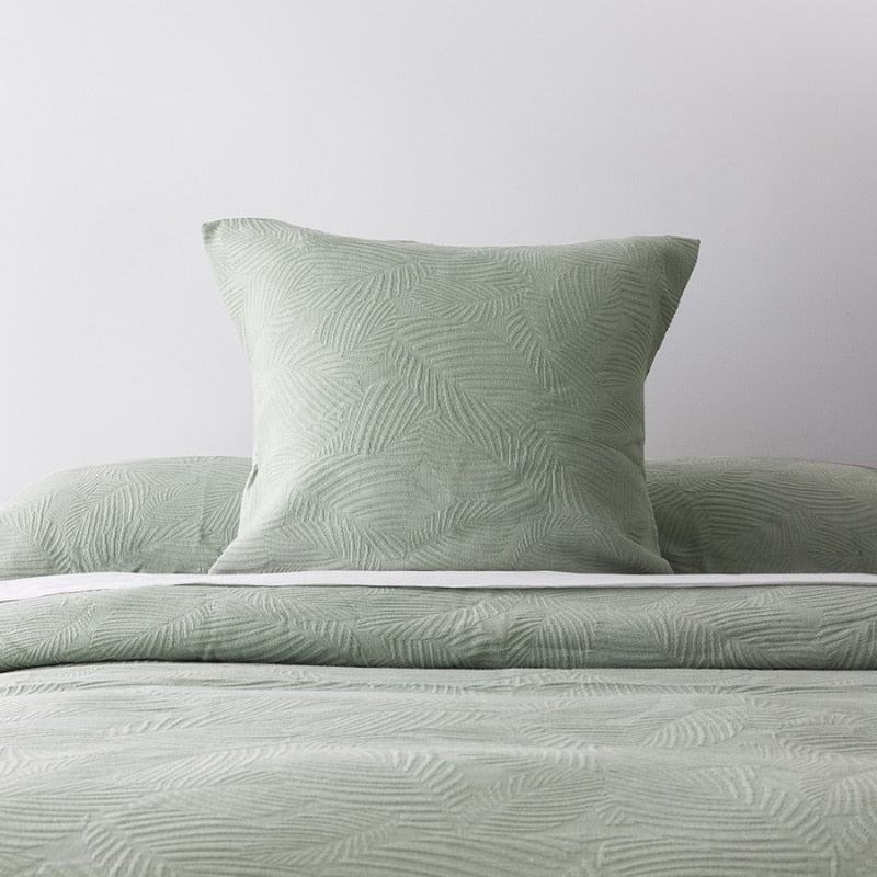 alt="A calming green tones european pillowcase featuring a subtle textural leaf pattern placed on top of a bed"