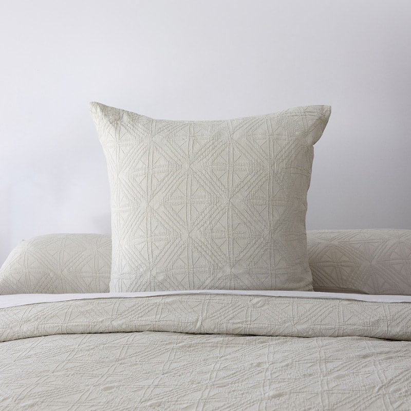 alt="A beautiful neutral stone colour european pillowcase featuring a geometric pattern placed on top of a bed"