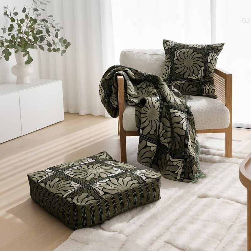 A stylish living room featuring a chair, table, and a Zinnia Floor Cushion in Moss with a floral design.