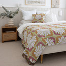 A bright floral Zinnia Multi Throw drapes over a bed, complemented by a nightstand, creating a warm and inviting bedroom setting.