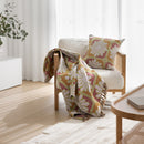 A white chair adorned with a vibrant yellow and pink throw, featuring the Bambury Zinnia Sorbet Cushion for added colour.