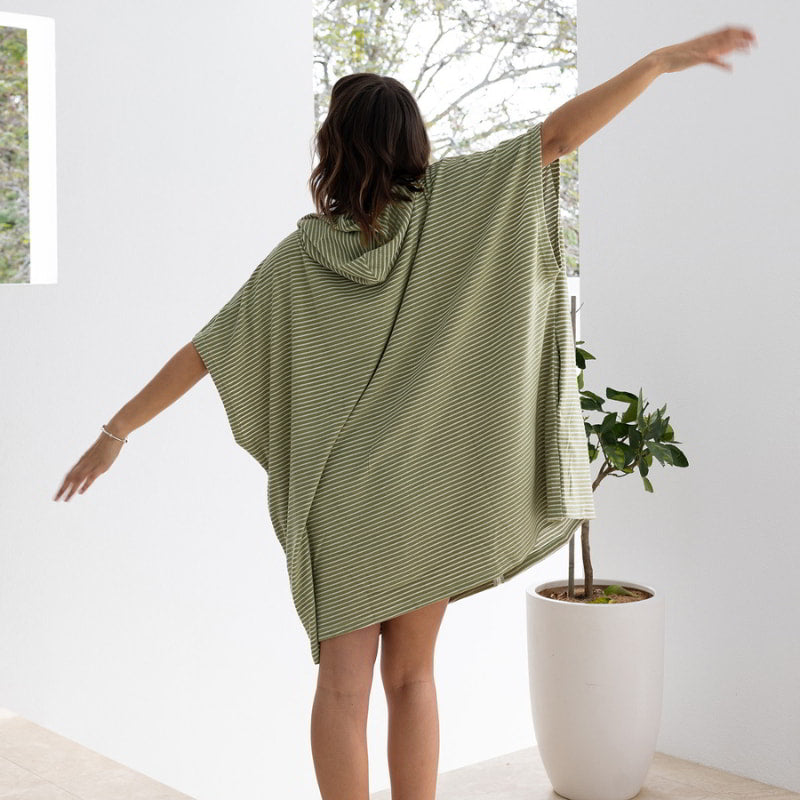 A woman with outstretched arms showcases her olive poncho, radiating comfort and warmth.
