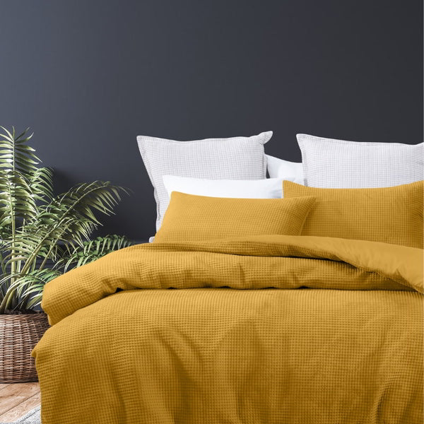 alt="A luxurious quilt cover set in a yellow hue will add cosiness to your bedroom."