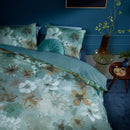 Front view of the Lou Blue Green Quilt Cover Set layered with light blue sheets in a blue-toned bedroom