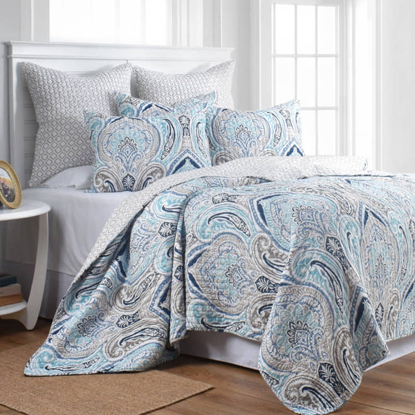 alt="A beautiful coverlet set designed with heritage flower and foliage pattern in blues and greys in a luxurious bedroom"