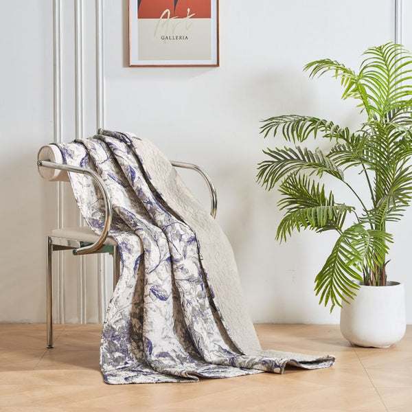 A 100% cotton throw featuring an intricate foliage and leaves in shades of blue and green on a textured background.