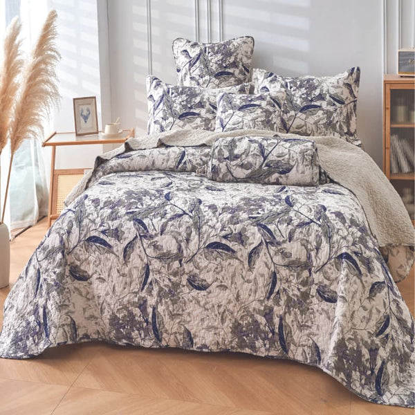 Serene blue and white coverlet set with pillows, showcasing lush foliage and leaves in shades of blue and green on a textured, crumpled background.