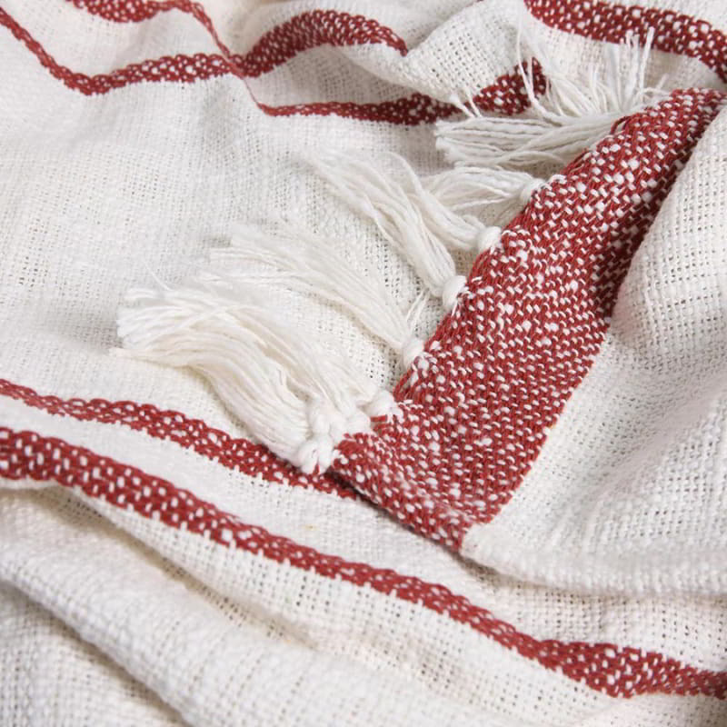 alt="Close up look of an ivory and brick throw with subtle stripe design and tassels"