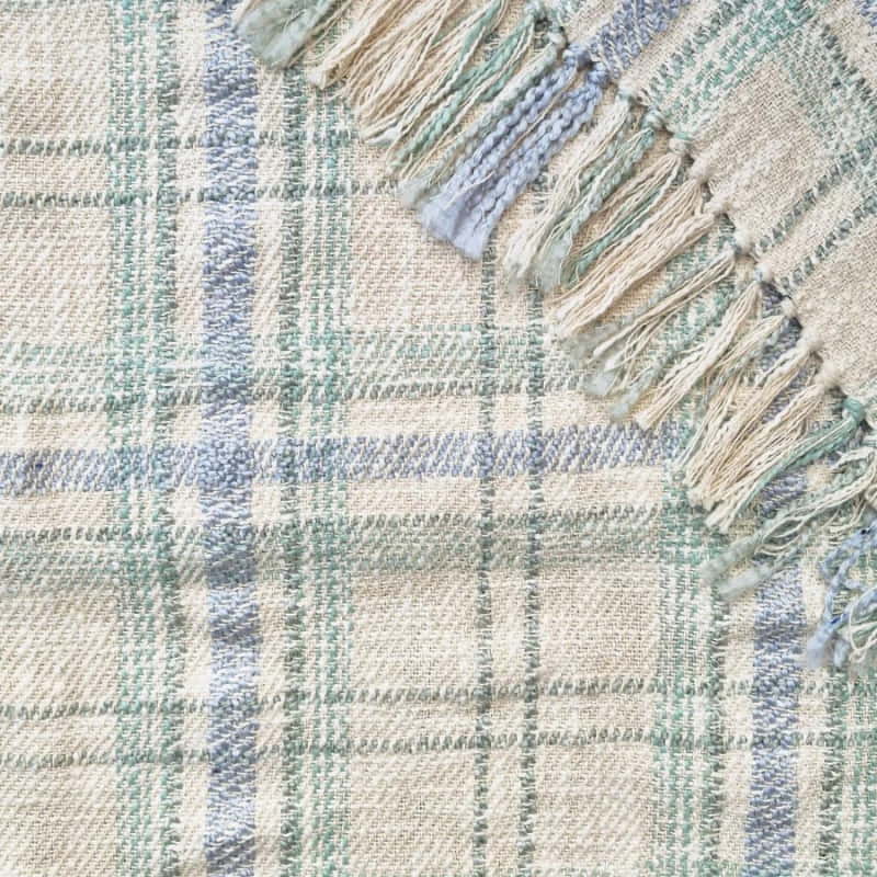 alt="Close-up details of a green multicoloured throw  featuring a playful check pattern weaved from different coloured string, with tassels on each side"