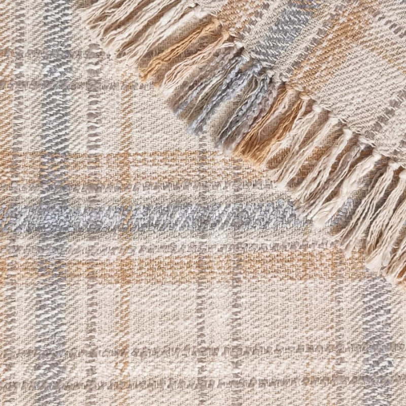 alt="Close-up details of a green multicoloured throw featuring a playful check pattern weaved from different coloured string, with tassels on each side"
