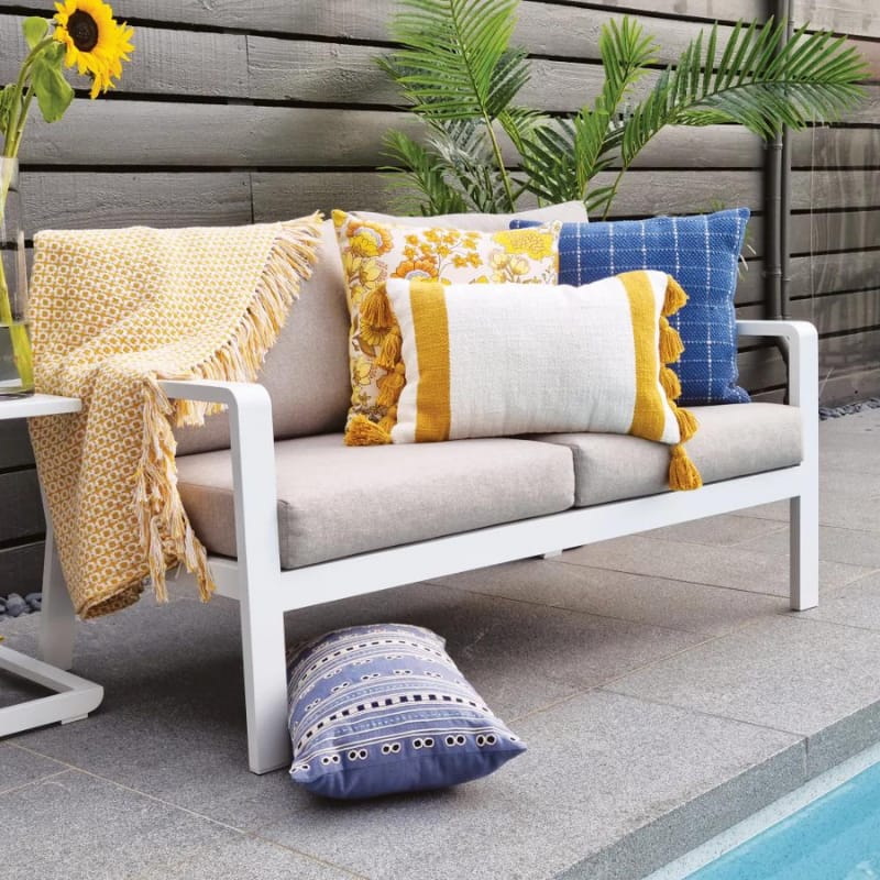 "A blue and cream check pattern cushion pairs with other collections of chic companion pillows in a cosy poolside setting"