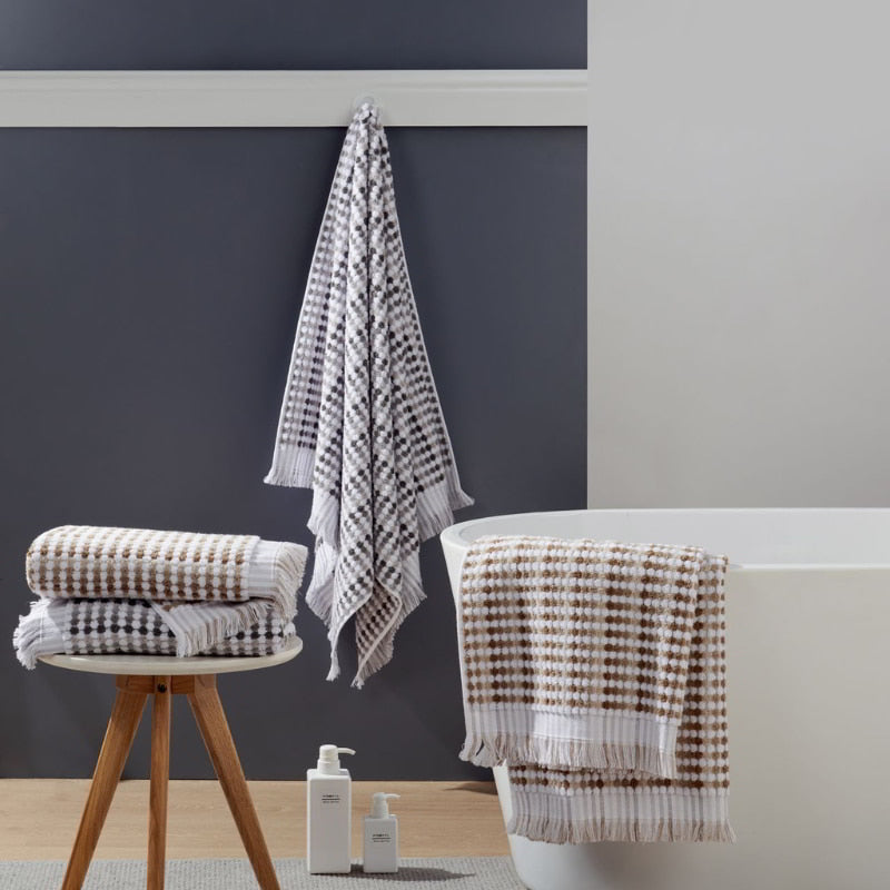 Elegant bathroom setup with a white tub, Jenny Mclean Pom Pom towels, and wooden stool, inviting relaxation and luxury.