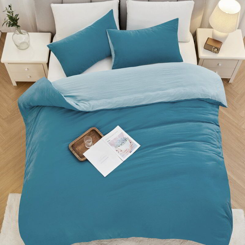 alt="Top view of a blue Linenova quilt cover set neatly laid on a bed, showcasing its elegant and soft appearance."