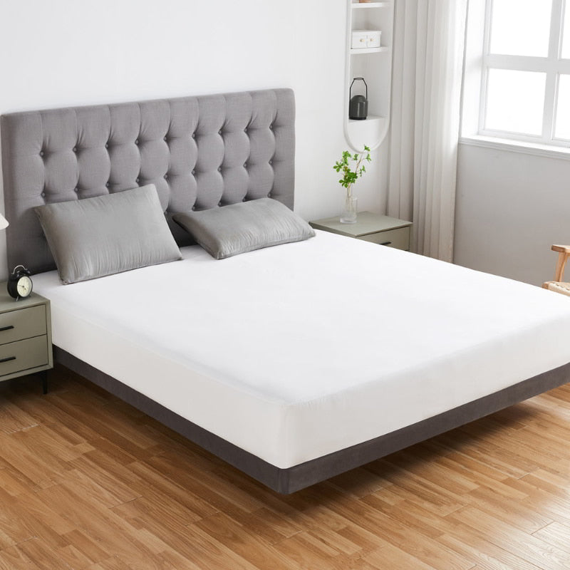 alt="A white fitted mattress protector, 100% waterproof and designed with a top-notch TPU layer, adds sophistication to the bedroom's appearance"