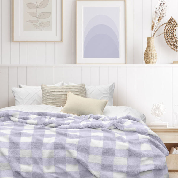 A luxurious bedroom with a lilac and white blanket featuring a large checkered pattern creates a bold visual grid, adding colour and pattern to the room's decor.