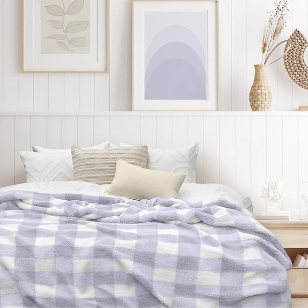 A luxurious bedroom with a lilac and white blanket featuring a large checkered pattern creates a bold visual grid, adding colour and pattern to the room's decor.