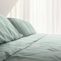 Bed with green and white striped sheet set, showcasing uniform horizontal stripes for a minimalist or nautical-themed bedroom decor.
