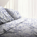 A lavender-toned bed sheets and pillows, adorned with a monochromatic white floral and foliage pattern, craft a serene and unique design on a cosy bedroom.