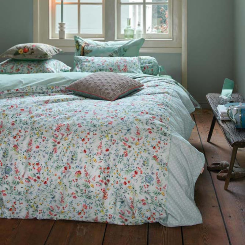 alt="Quilt cover with delicate all-over floral print and reversible stylized tile pattern in a cosy bedroom."