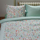 alt="Close up look of a quilt cover with delicate all-over floral print and reversible stylized tile pattern in a cosy bedroom."