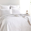 alt-"Showcasing a white coverlet draws inspiration from the ornate detailing of traditional Greek tile patterns pairing with the pillows in a cosy bedroom"