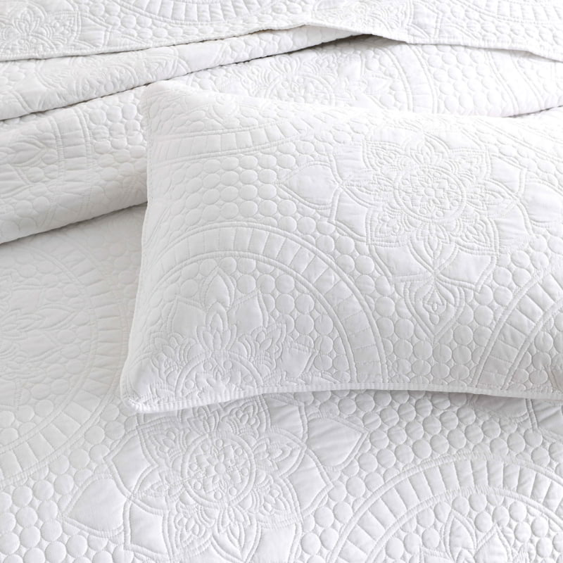 alt-"A white coverlet draws inspiration from the ornate detailing of traditional Greek tile patterns in a luxurious bedroom"