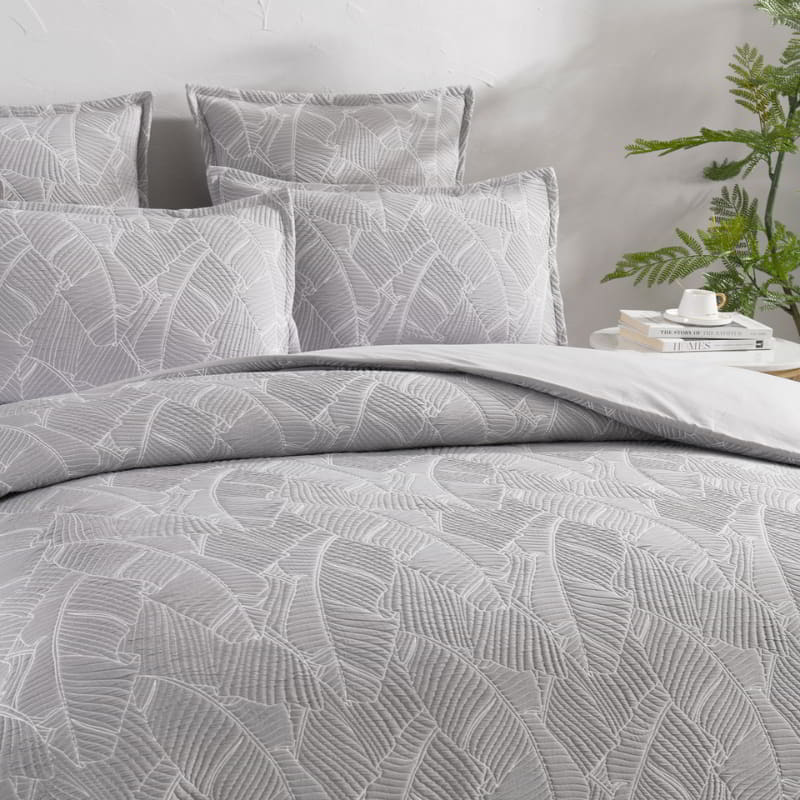 alt="Close-up look of a grey and white quilt cover, neutral-toned with a tropical banana leaf design, perfect for a boho look."
