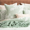 A sumptuous bed, embellished with soft pillows and a sage green blanket, accompanied by a european pillowcase adorned with a charming floral design.