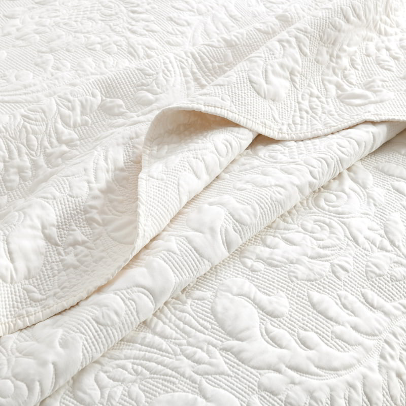 alt="Closer look of a luxurious coverlet featuring a damask woven style fabric and intricate textile in a cosy bedroom."