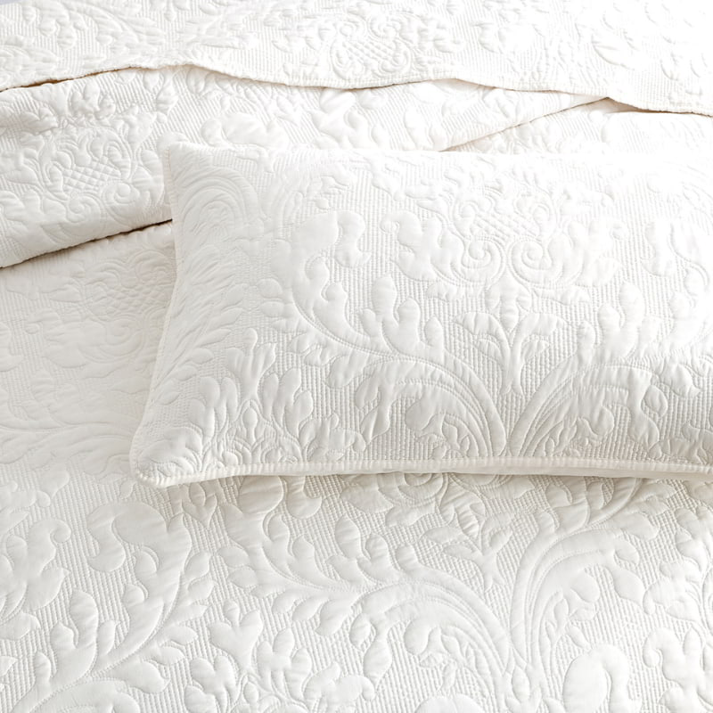 alt="Elegant white bed with quilt and pillows, showcasing a luxurious damask woven style fabric."