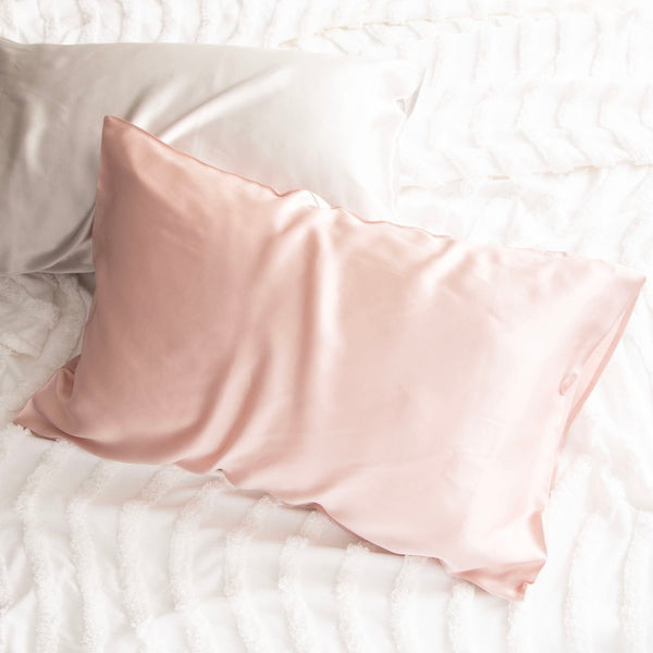 alt="Pink and light brown pillowcase on a white bed. Crafted from 100% pure mulberry silk, these luxurious pillows offer a refreshing experience for your skin. "