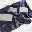 alt="A navy satin standard pillowcase, and eye mask made from 100% pure mulberry silk."