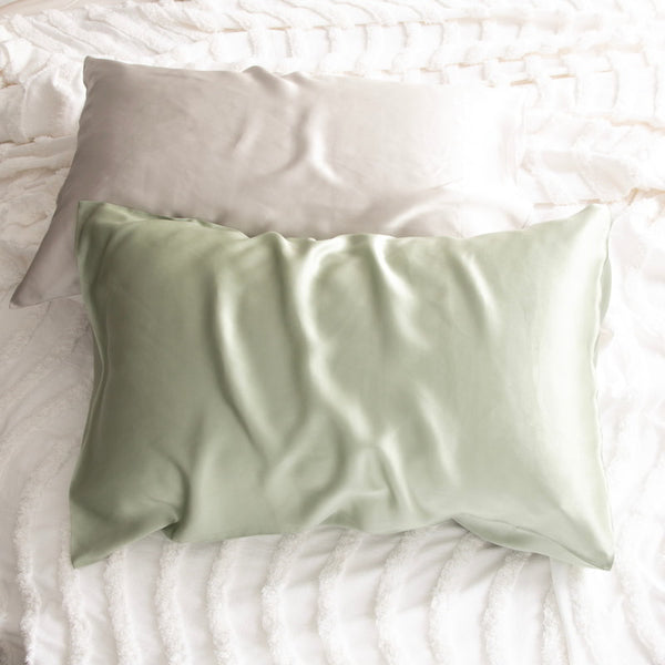 alt="Light brown and green pillowcase on a white bed. Crafted from 100% pure mulberry silk, these luxurious pillows offer a refreshing experience for your skin. "