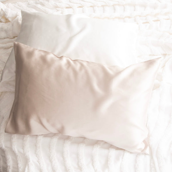 alt="A shade of white and sand pillowcase on a white bed. Crafted from 100% pure mulberry silk, these luxurious pillows offer a refreshing experience for your skin. "