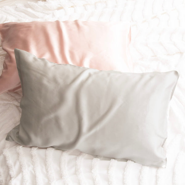 alt="Pink and silver pillowcase on a white bed. Crafted from 100% pure mulberry silk, these luxurious pillows offer a refreshing experience for your skin. "