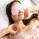 alt="The pink silk eye mask wore by the woman is made from 100% pure mulberry silk with six layers of padding. Wake up refreshed with this gentle mask."
