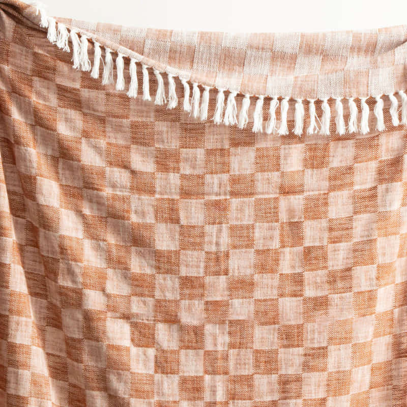 Flat lay of the Renee Taylor Nevis terracotta checkered throw with white fringe

