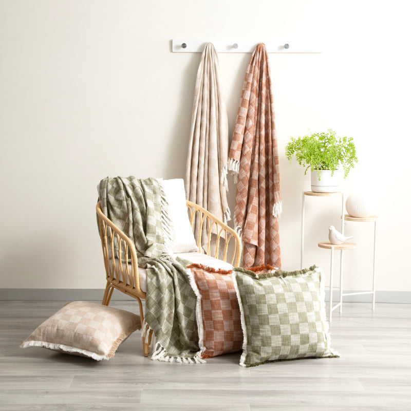 Terracotta and green checkered throws styled with matching cushions in a rattan chair setup