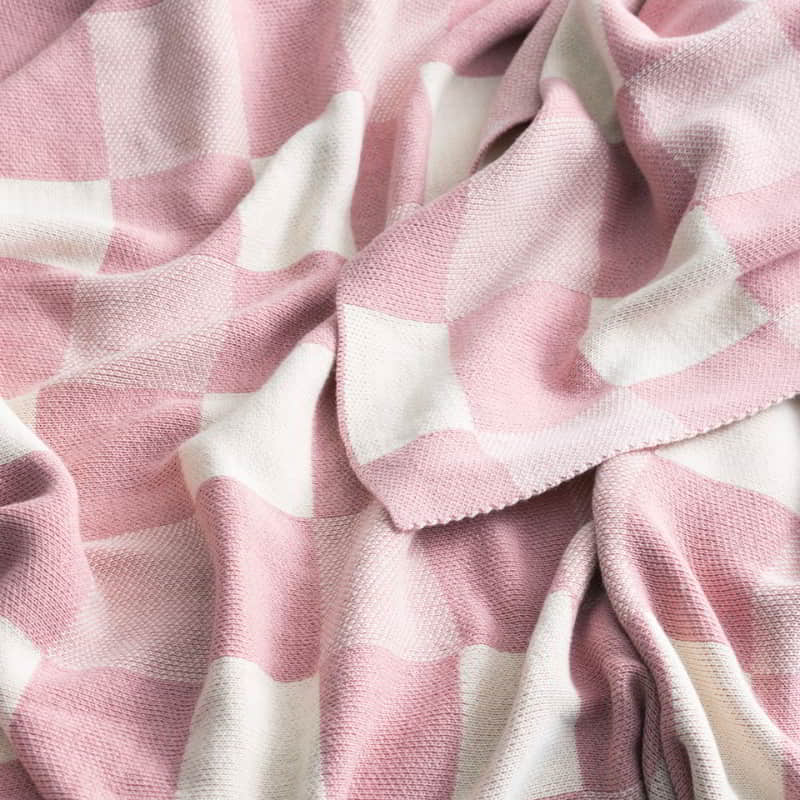 alt="Close-up details of a meticulously crafted pink and white blanket with large checkered pattern. Made of high-quality cotton knit for durability and comfort."