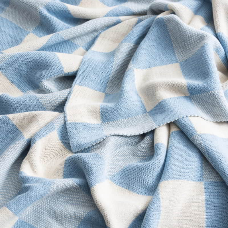 alt="Zoom in details of a yarn-dyed cotton knitted blanket with large checks design in French blue. Ultra-soft and cosy texture, perfect for any decor style."