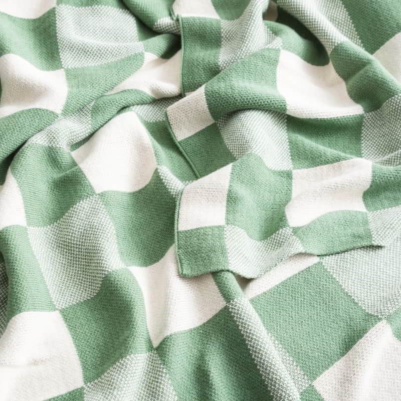 alt="Zoom in details of a shade of green with a yarn-dyed cotton knitted blanket with large checks design in French blue. Ultra-soft and cosy texture, perfect for any decor style."